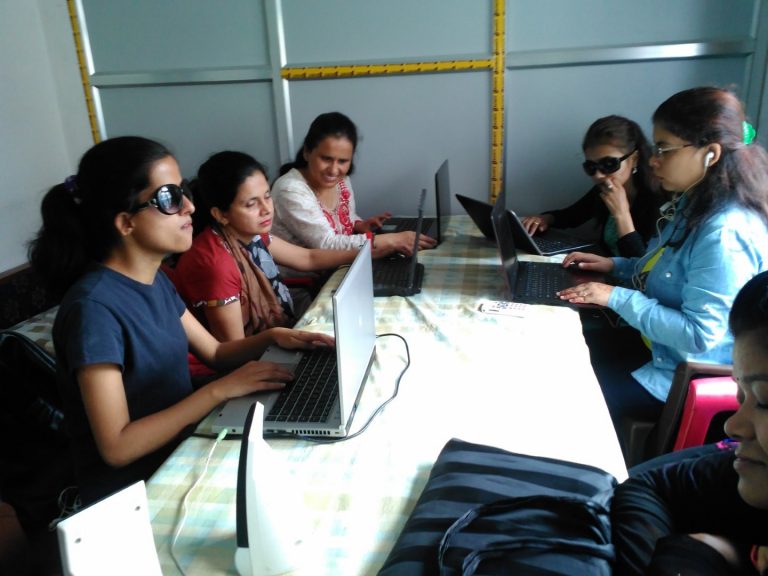A group of ladies is seen using the laptop sitting around a table