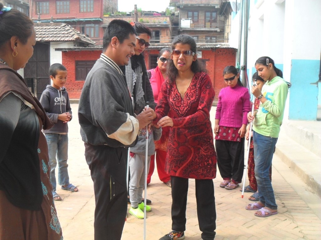 A lady is giving a white cane to a visually impaired person.
