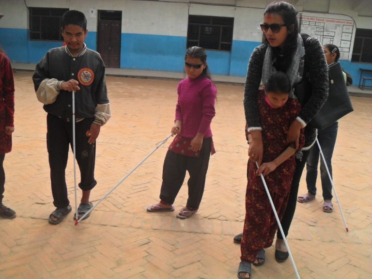 The trainer is guiding a little girl on how to use the white cane.