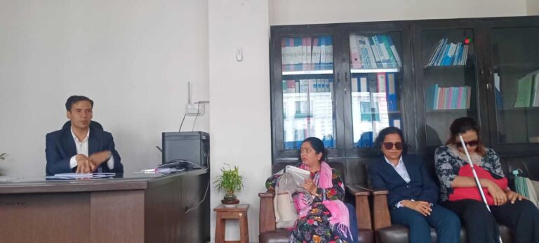 5Three women from representative organizations and Mr. Gyan Mani Ghimire are in an office. Mr. Ghimire is sitting behind a desk with his hands gesturing, indicating he is speaking. The three women are seated on a couch to his right, and one of them is holding a white cane.