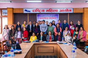 A group photo taken at the end of the program. In the front row, several key representatives and dignitaries are seated together at the conference table. Behind them, other participants—mostly women, including women with disabilities stand in rows, smiling toward the camera.